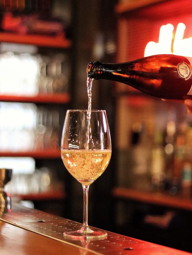 Vin spumant turnat în pahar, cu neonul barului în fundal
